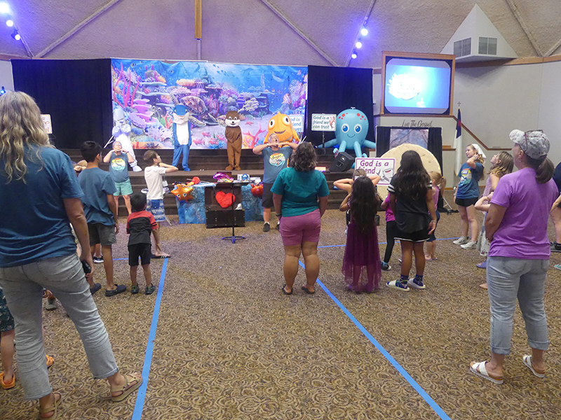 Kids and Volunteers at VBS looking at Mascots on stage